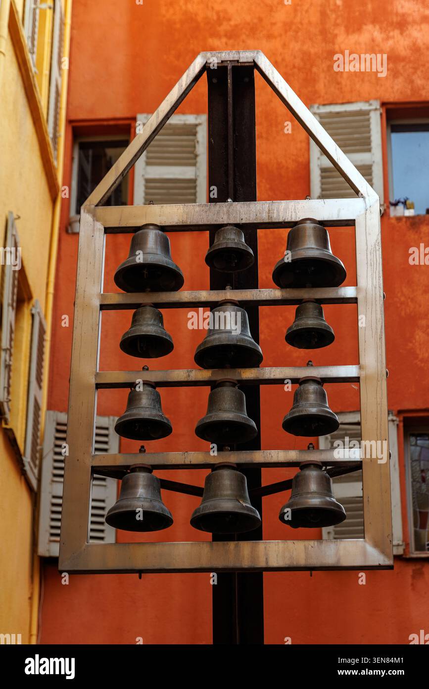 Una cornice verticale di dodici campane in bronzo o ferro disposte in un telaio geometrico in metallo. L'installazione è impostata all'esterno tra i tradizionali colori r Foto Stock