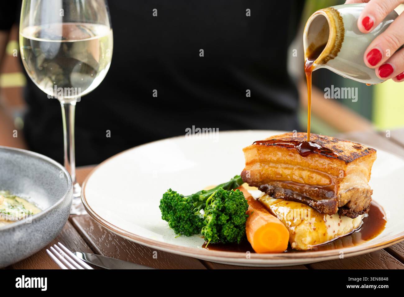 Gustosi pancetta di maiale condita con salsa ricca servita in un elegante ambiente all'aperto Foto Stock