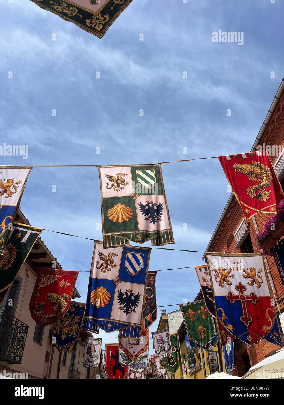 Striscioni araldiche e pennant in stile medievale che espongono stemmi con leoni e croci appesi sopra una strada durante una festa medievale in Spagna - Immagine stock catturata con smartphone