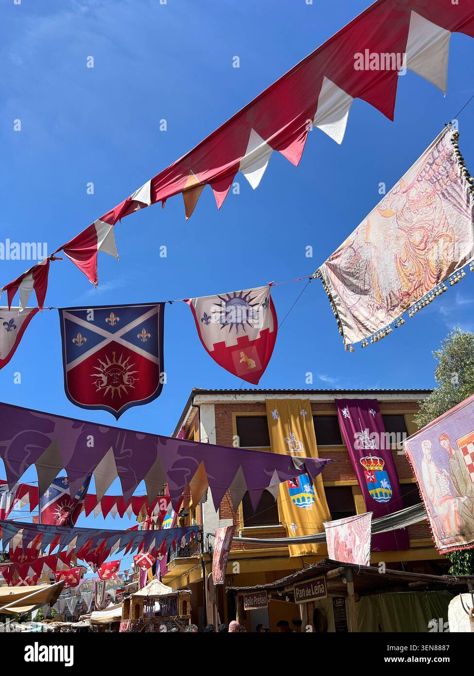 Striscioni araldiche e pennant in stile medievale che espongono stemmi con leoni e croci appesi sopra una strada durante una festa medievale in Spagna - Immagine stock catturata con smartphone