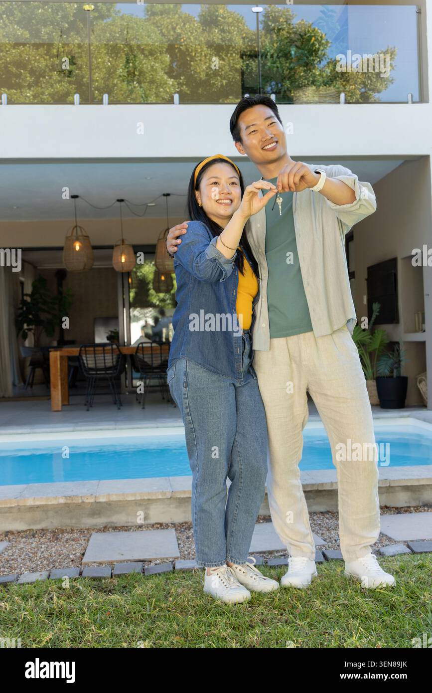 Coppie diverse in piedi sul prato a bordo piscina tenendo il portachiavi e sorridendo vicino al tavolo da pranzo in legno Foto Stock