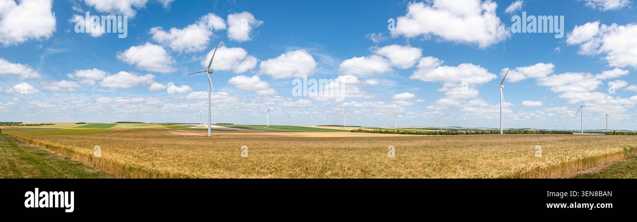 Vista panoramica delle turbine eoliche in un campo di grano nella campagna francese con un cielo blu punteggiato da piccole nuvole bianche. Concetto di energia rinnovabile Foto Stock