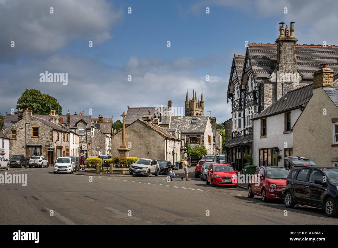 Ampia e ampia vista del paesaggio che guarda attraverso la strada principale curvilinea e la piazza centrale del villaggio verso la lontana guglia della chiesa a Tideswell, Derbyshire Foto Stock