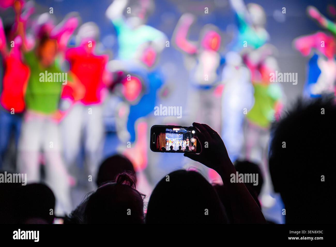 Tieni lo smartphone a mano per catturare un luminoso spettacolo dal vivo con ballerini sfocati sullo sfondo Foto Stock