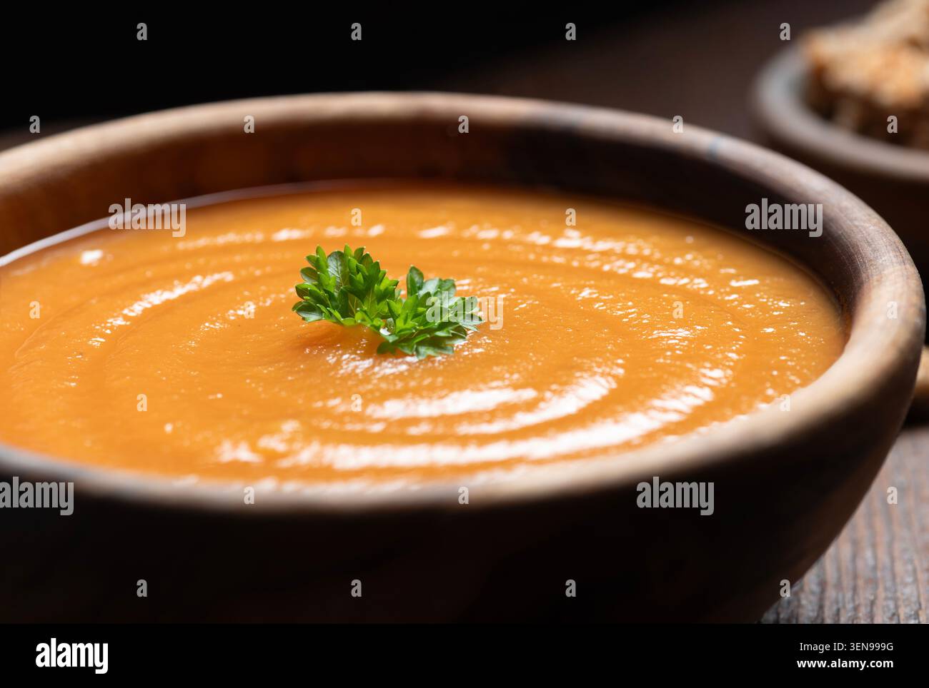 Una minestra fresca di gazpacho servita in una ciotola rustica di legno e guarnita con prezzemolo fresco. Zuppa di cibo estivo spagnolo con consistenza liscia, colori vivaci e. Foto Stock