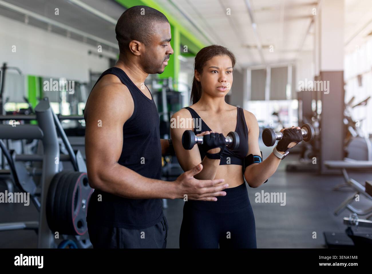Personal trainer che coaching giovane donna che esegue ricci stupidi nel moderno fitness club Foto Stock