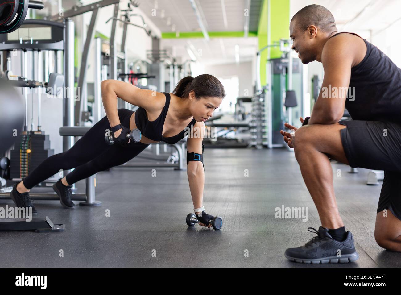 Donna che fa esercizio con manubri e personal trainer in palestra Foto Stock