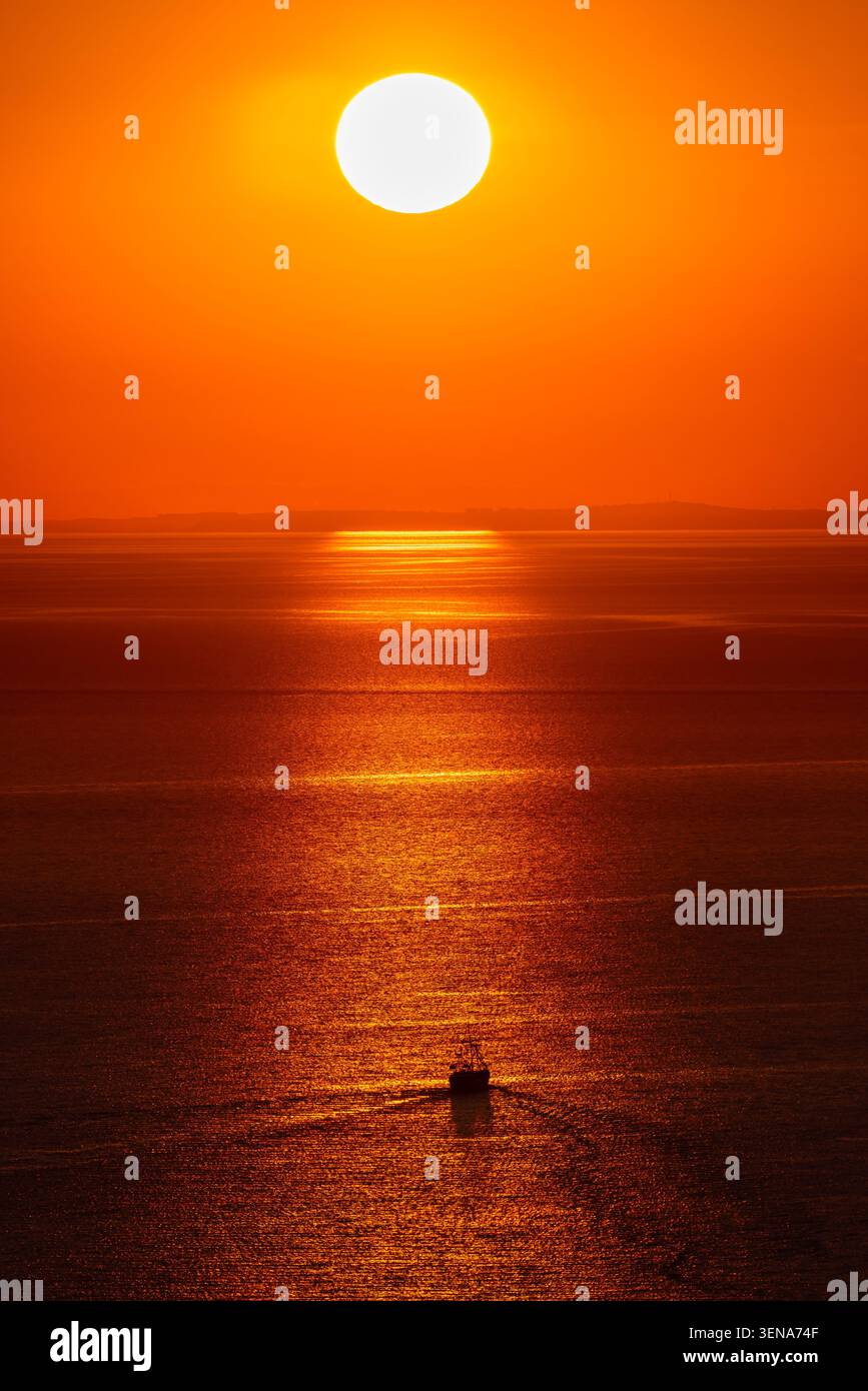 Barca sotto il sole luminoso sul mare calmo con lo spettacolare tramonto arancione Foto Stock