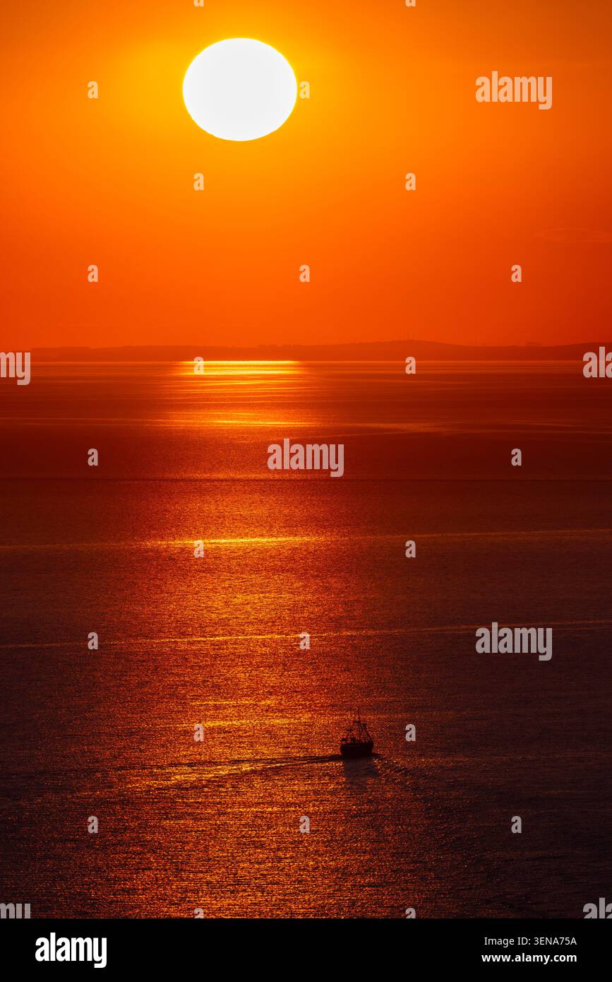 Barca sotto il sole luminoso sul mare calmo con lo spettacolare tramonto arancione Foto Stock