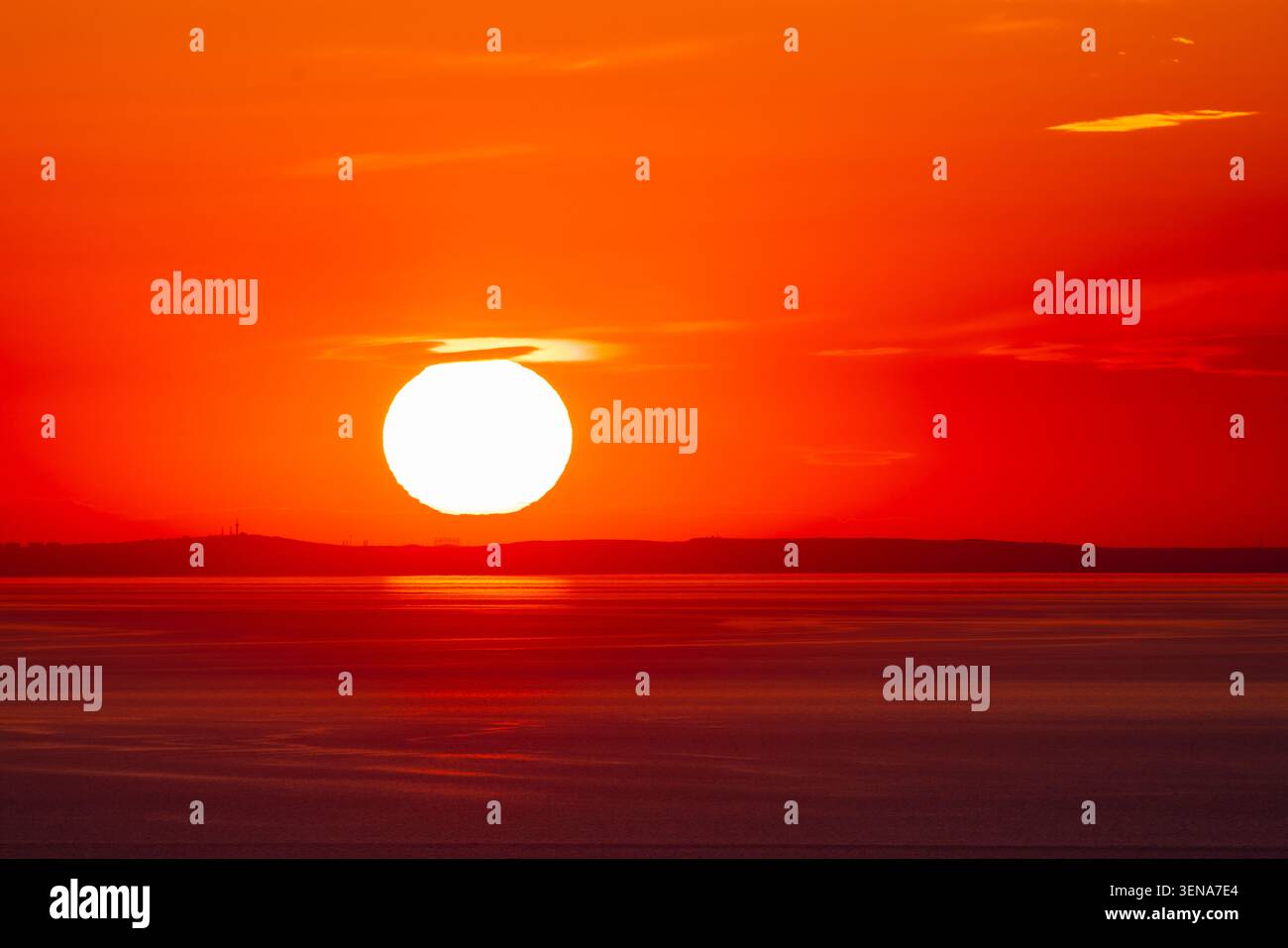 Enorme sole arancione che tramonta sul mare calmo e sull'orizzonte lontano Foto Stock