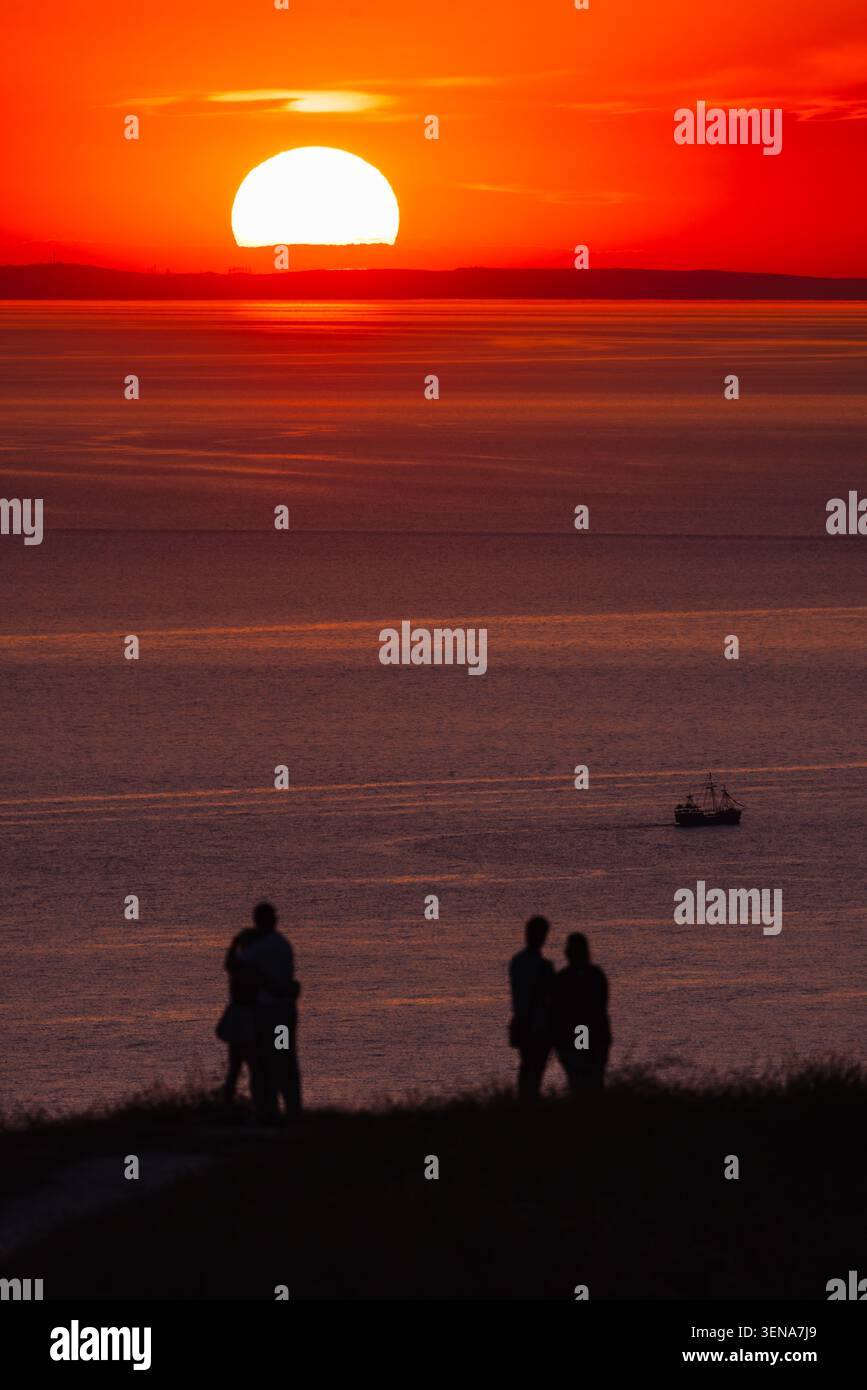 Sagome di gruppo che si godono il tramonto sul tranquillo orizzonte dell'oceano Foto Stock