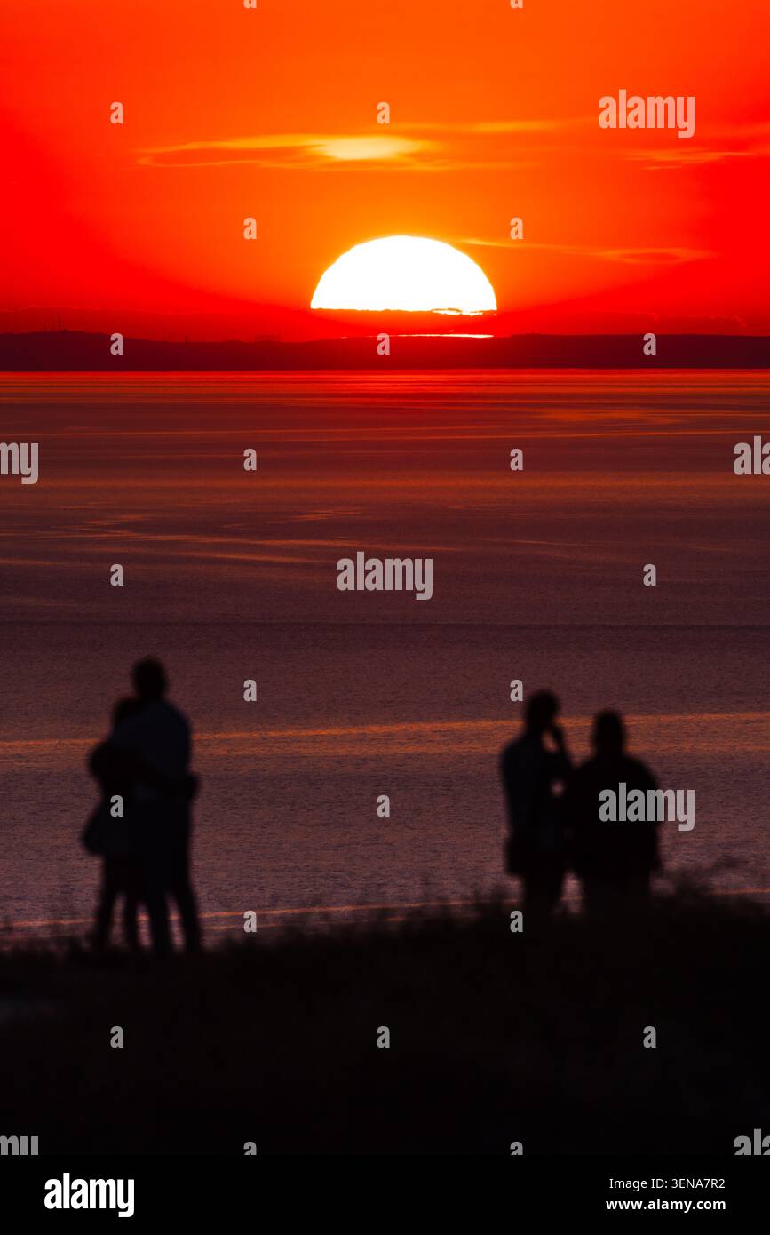 Silhouette romantiche vicino al mare al tramonto con un cielo arancione scintillante Foto Stock