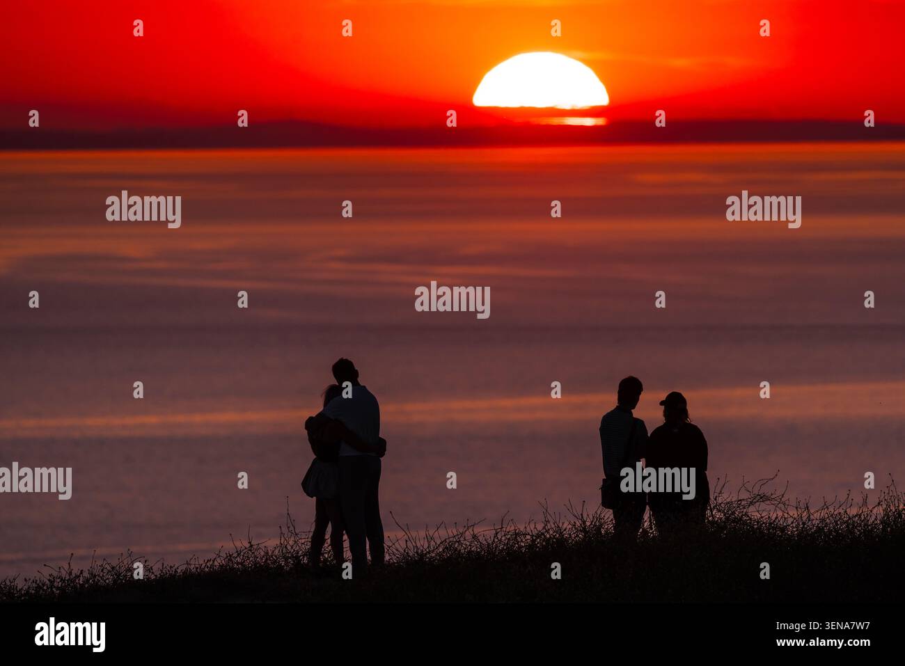 Sagome di gruppo che si godono il suggestivo tramonto sull'orizzonte del mare Foto Stock