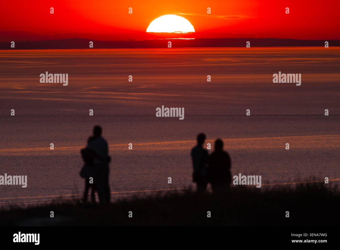 Persone che guardano il tramonto infuocato sull'oceano calmo con il cielo serale colorato Foto Stock