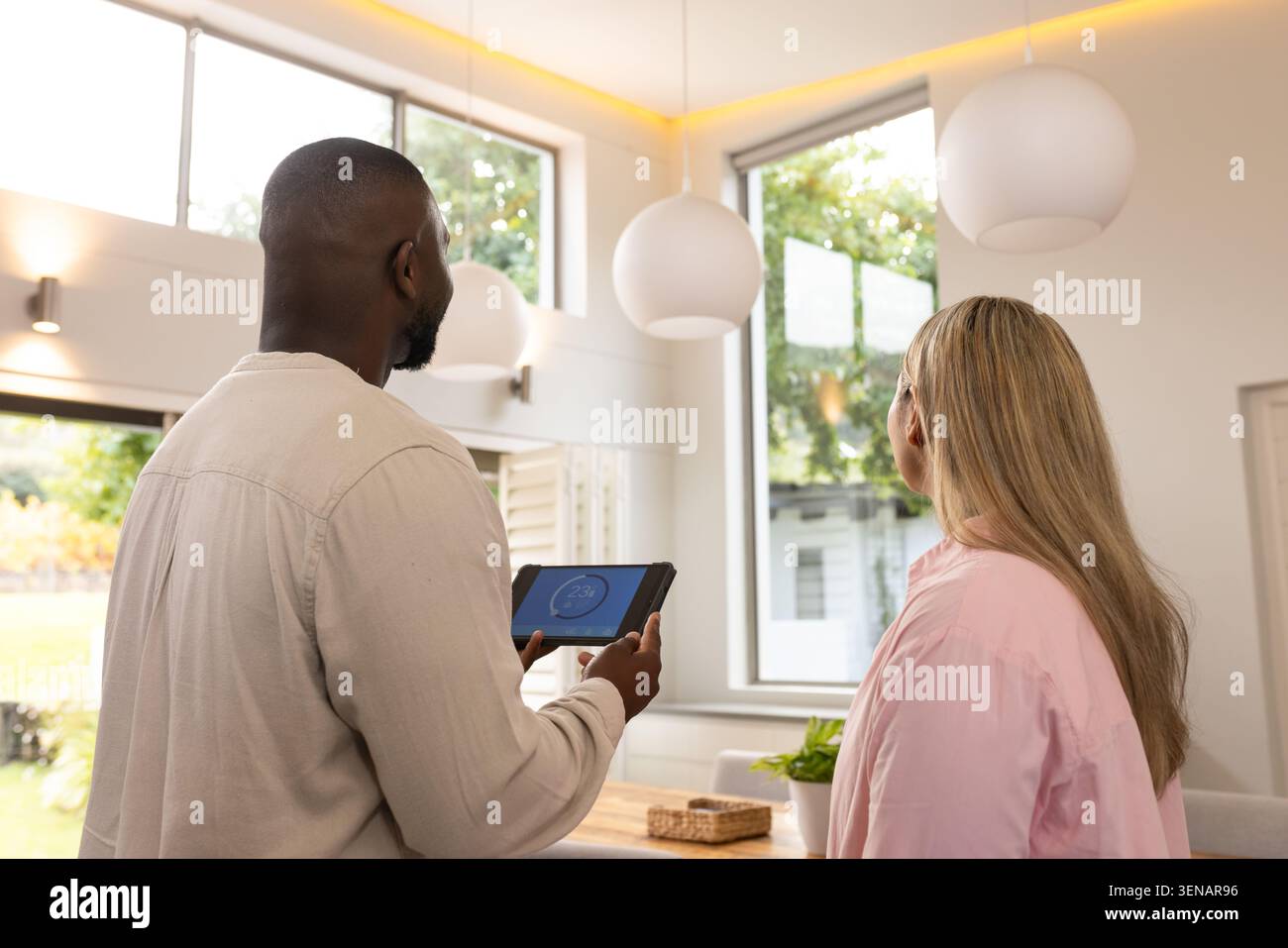 Diversi adulti che esaminano tablet con calibro circolare, in piedi in una moderna sala da pranzo vicino alle finestre Foto Stock
