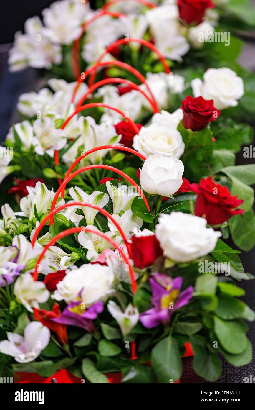 Una fila di eleganti composizioni floreali con rose rosse e bianche fresche, alstroemeria e fiori viola in cesti regalo con manici rossi. Foto Stock