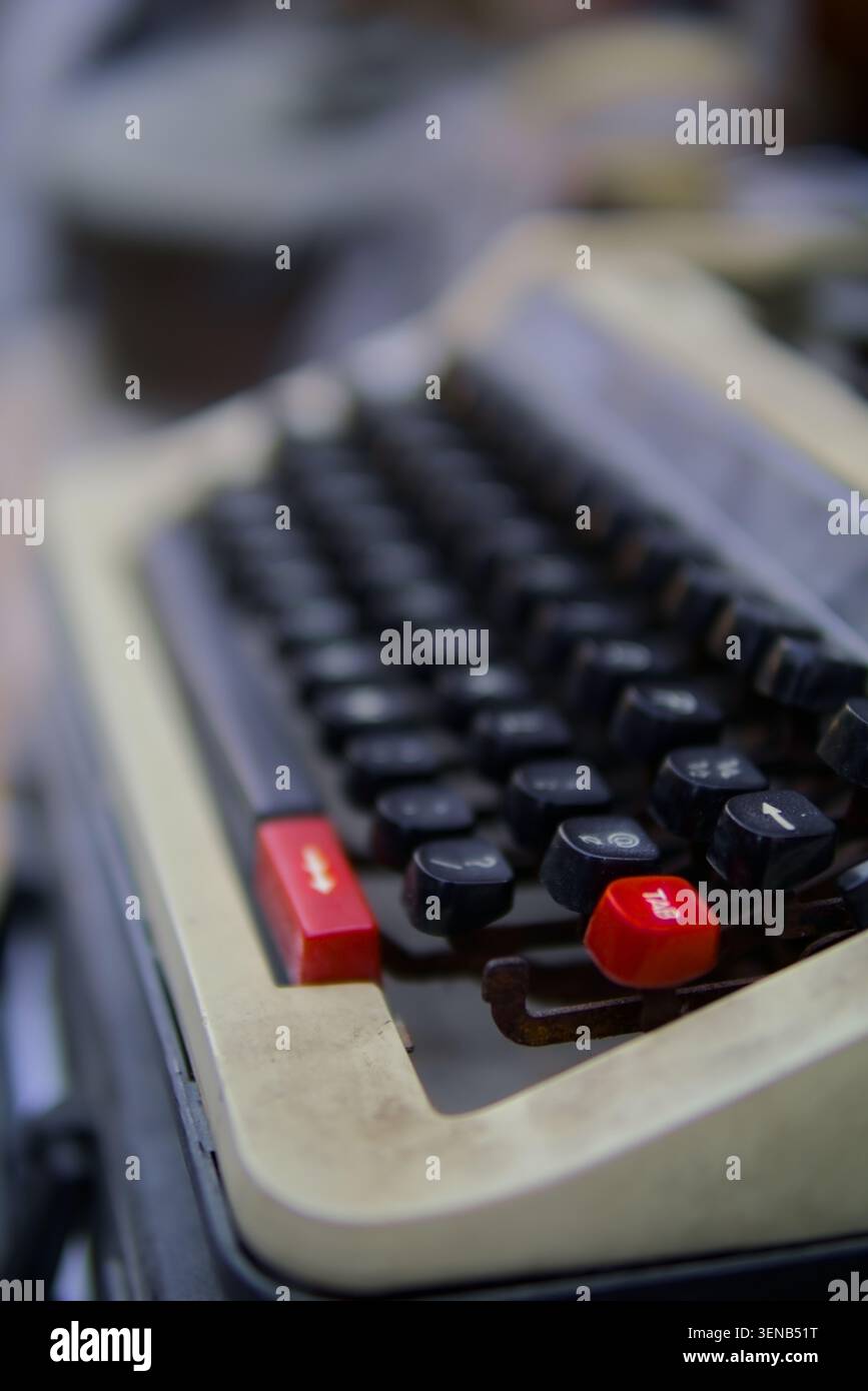 La macchina da scrivere vintage con tasti rossi risplende delicatamente. La messa a fuoco morbida mette in risalto i tasti usurati e il design classico. Il sentimento nostalgico evoca la scrittura e il creat della vecchia scuola Foto Stock