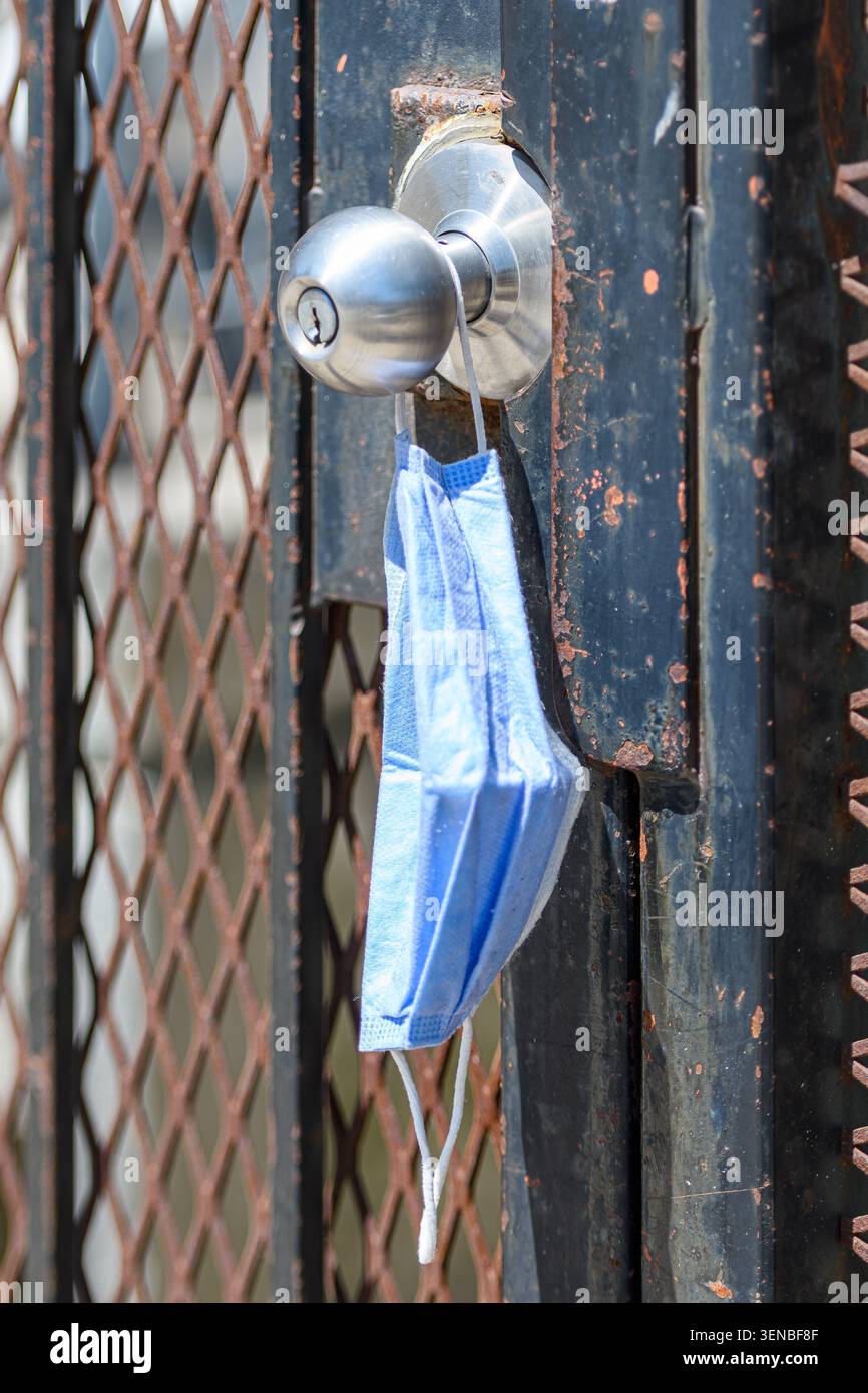 Maschera facciale usa e getta appesa da una maniglia di porta di cancello in metallo come residuo urbano abbandonato. Foto Stock