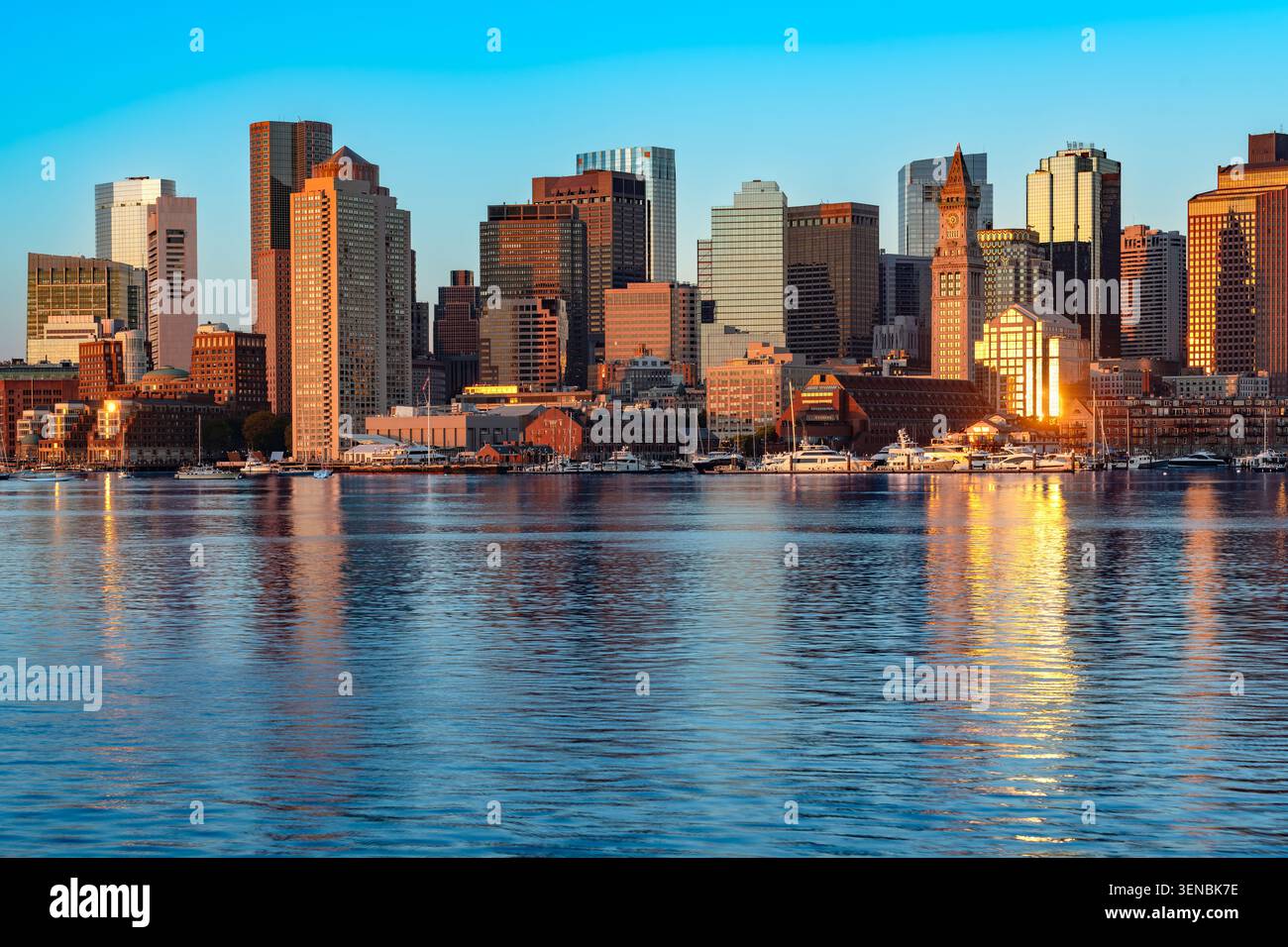 Un'ampia vista sulla baia da East Boston cattura lo skyline del centro di Boston all'alba con l'acqua che riflette la calda luce dorata sulla città. Foto Stock