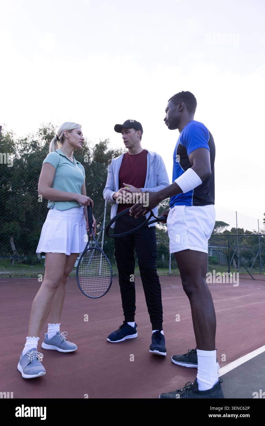 Gruppo di due uomini e una donna in piedi sul campo da tennis rosso con racchette Foto Stock