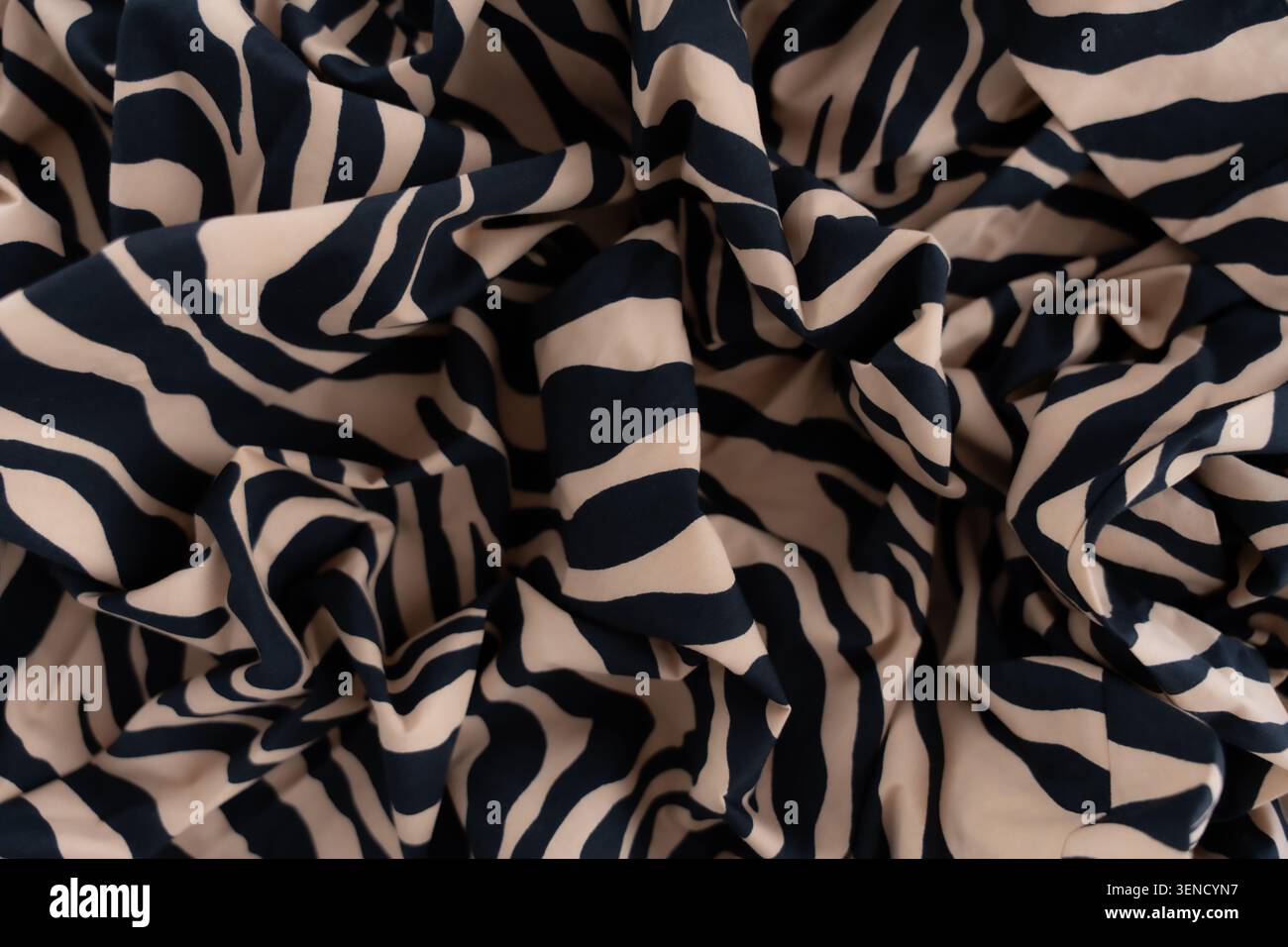 Primo piano del tessuto stampato zebra beige e nero con pieghe morbide e motivo astratto, messa a fuoco selettiva Foto Stock