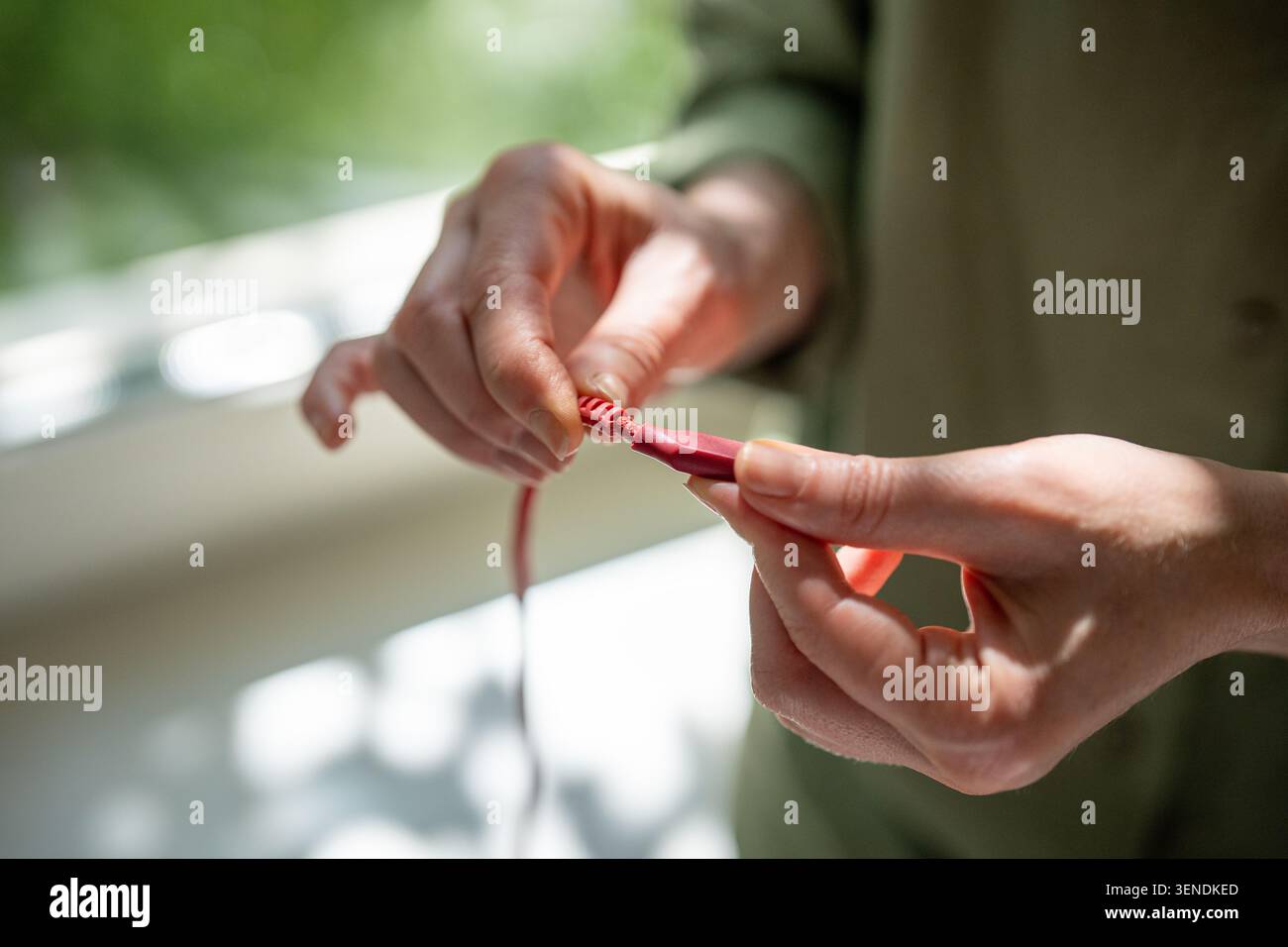 Donna che tiene le mani mostrando il cavo di ricarica dello smartphone con avvolgimento danneggiato vicino al collegamento della spina Foto Stock