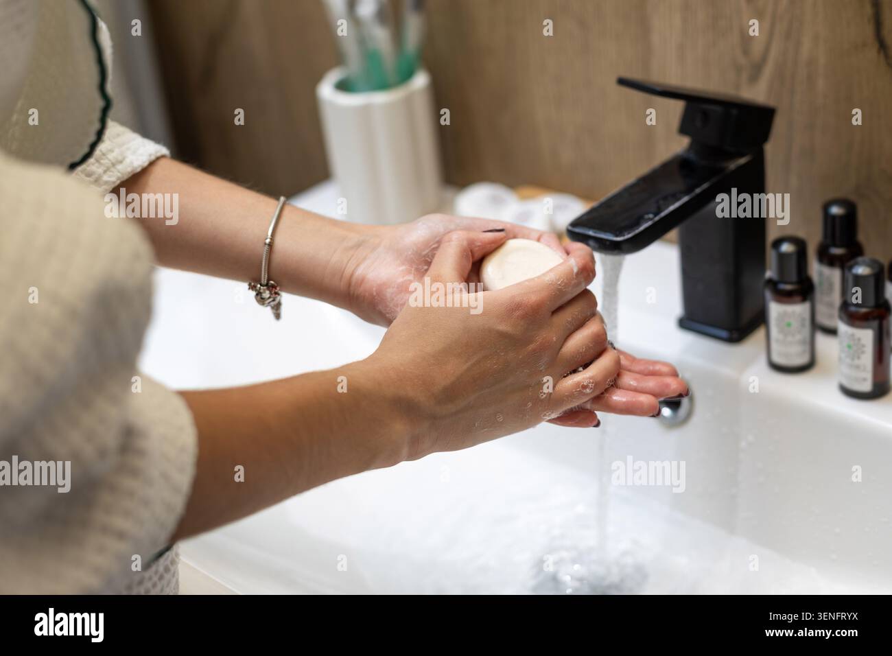 Donna che lava le mani con sapone al lavello del bagno. Primo piano di una donna che si lava le mani con una barretta rotonda di sapone sotto l'acqua corrente in un bagno bianco Foto Stock