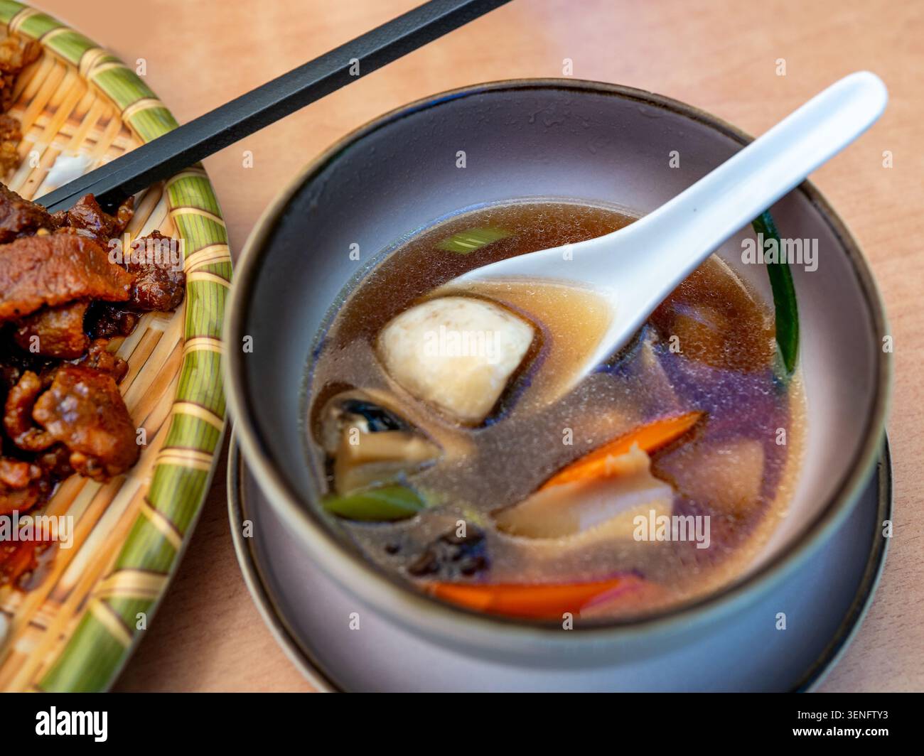 Zuppa asiatica piccante con funghi e verdure nel piatto sul tavolo. Parte del piatto con pezzetti di pollo in salsa di soia, bacchetta, primo piano. Foto Stock