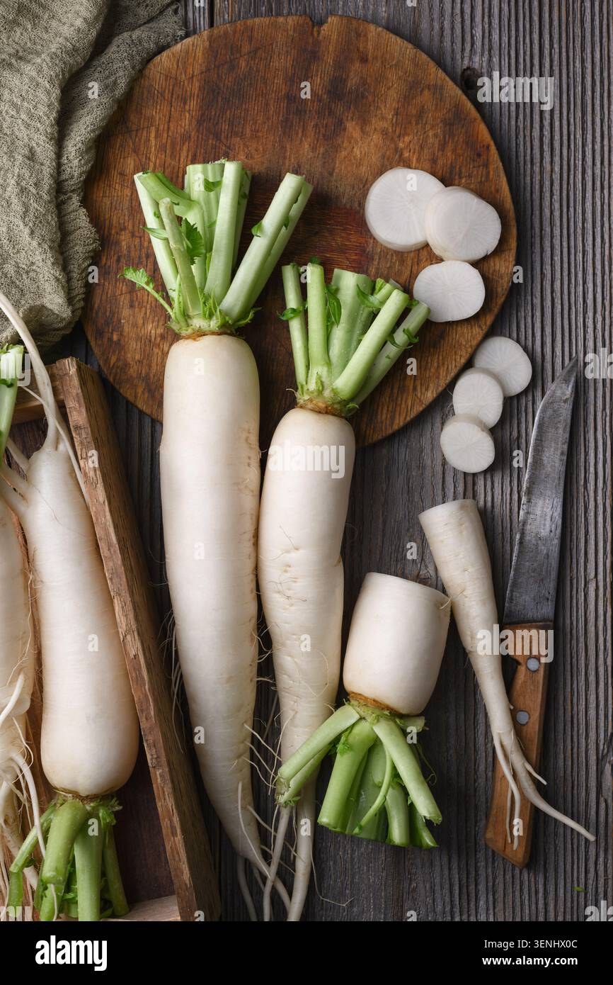 Ravanello daikon intero e a fette su superficie in legno, ravanello bianco, verdure biologiche Foto Stock