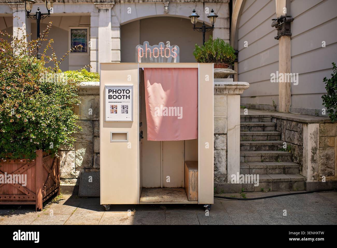 Batumi, Georgia - 9 giugno 2026: Cabina fotografica all'aperto in stile retrò con insegna al neon e sipario rosa su una strada soleggiata della città. Foto Stock