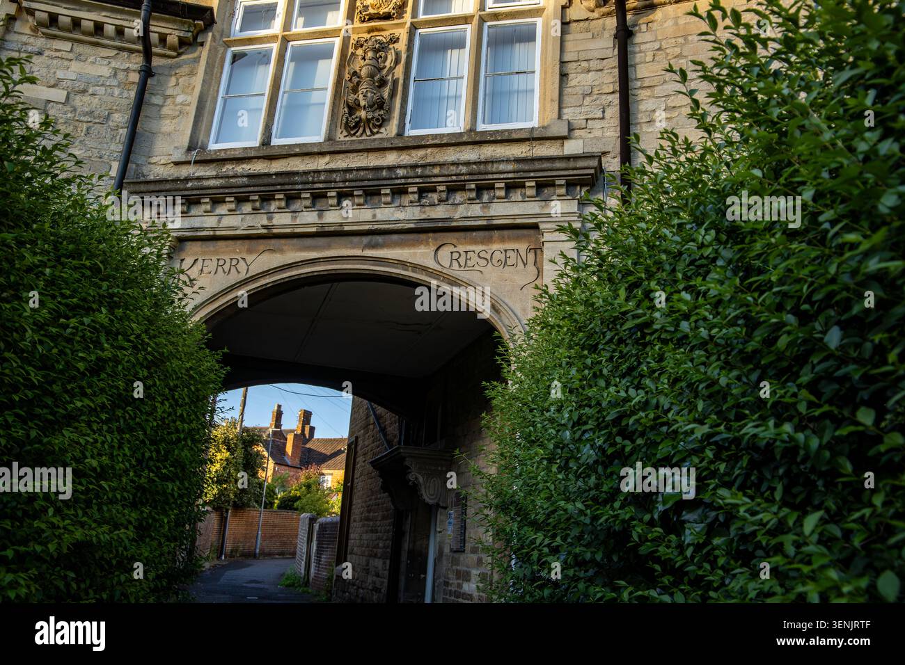 Un'entrata ad arco in pietra chiamata Kerry Crescent con intagli in pietra ornamentali e finestre sopra circondate da siepi verdi di Calne Wiltshire Foto Stock