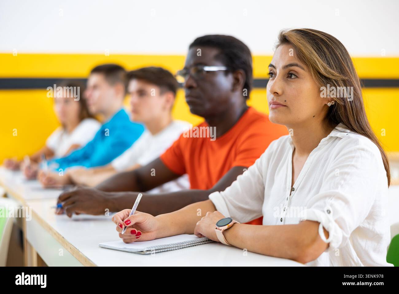 Donne e uomini seduti alla scrivania in classe che lavorano durante le lezioni di educazione per adulti Foto Stock