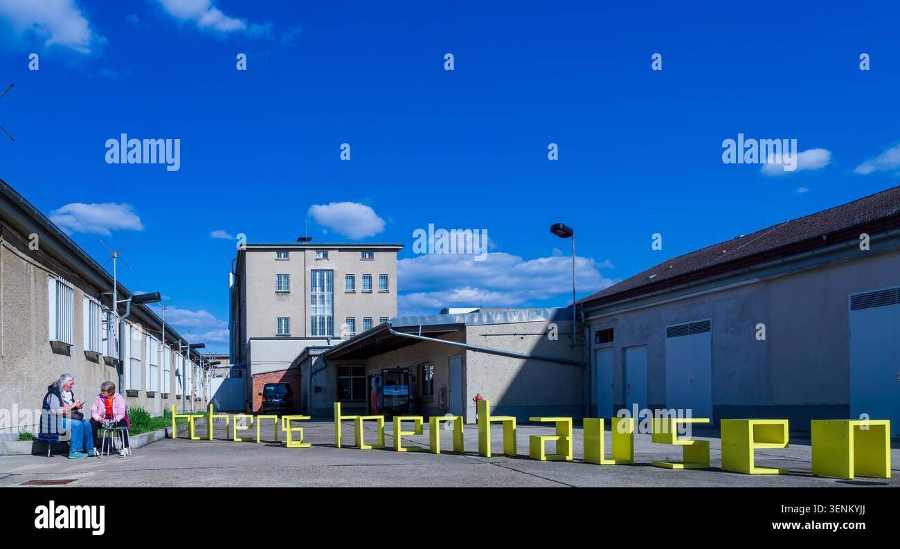 I visitatori si rilassano nel cortile del Memoriale di Berlino-Hohenschönhausen accanto all'installazione gialla dei posti a sedere "Hohenschönhausen", Gedenkstätte. Foto Stock