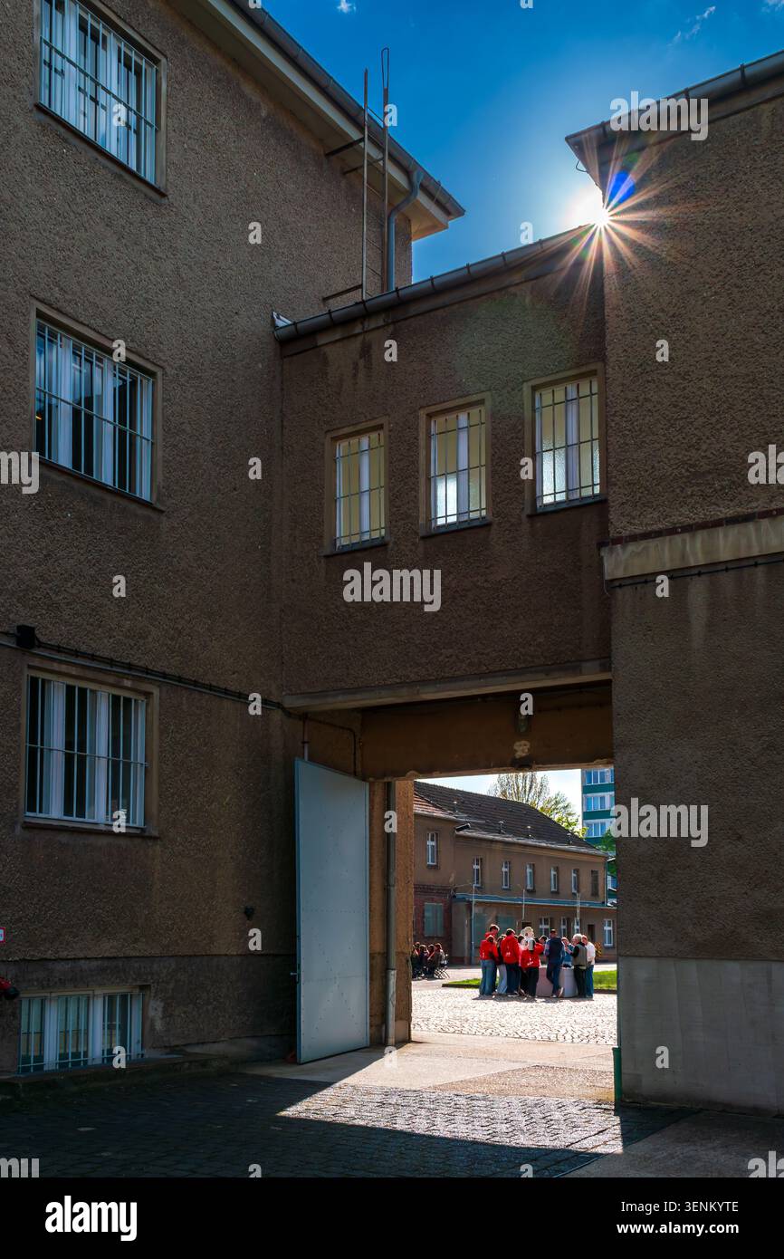 La luce del sole splende attraverso un cancello aperto al Memoriale di Berlino-Hohenschönhausen mentre un gruppo di studenti si riunisce nel cortile del modulo. Prigione della Stasi. Foto Stock