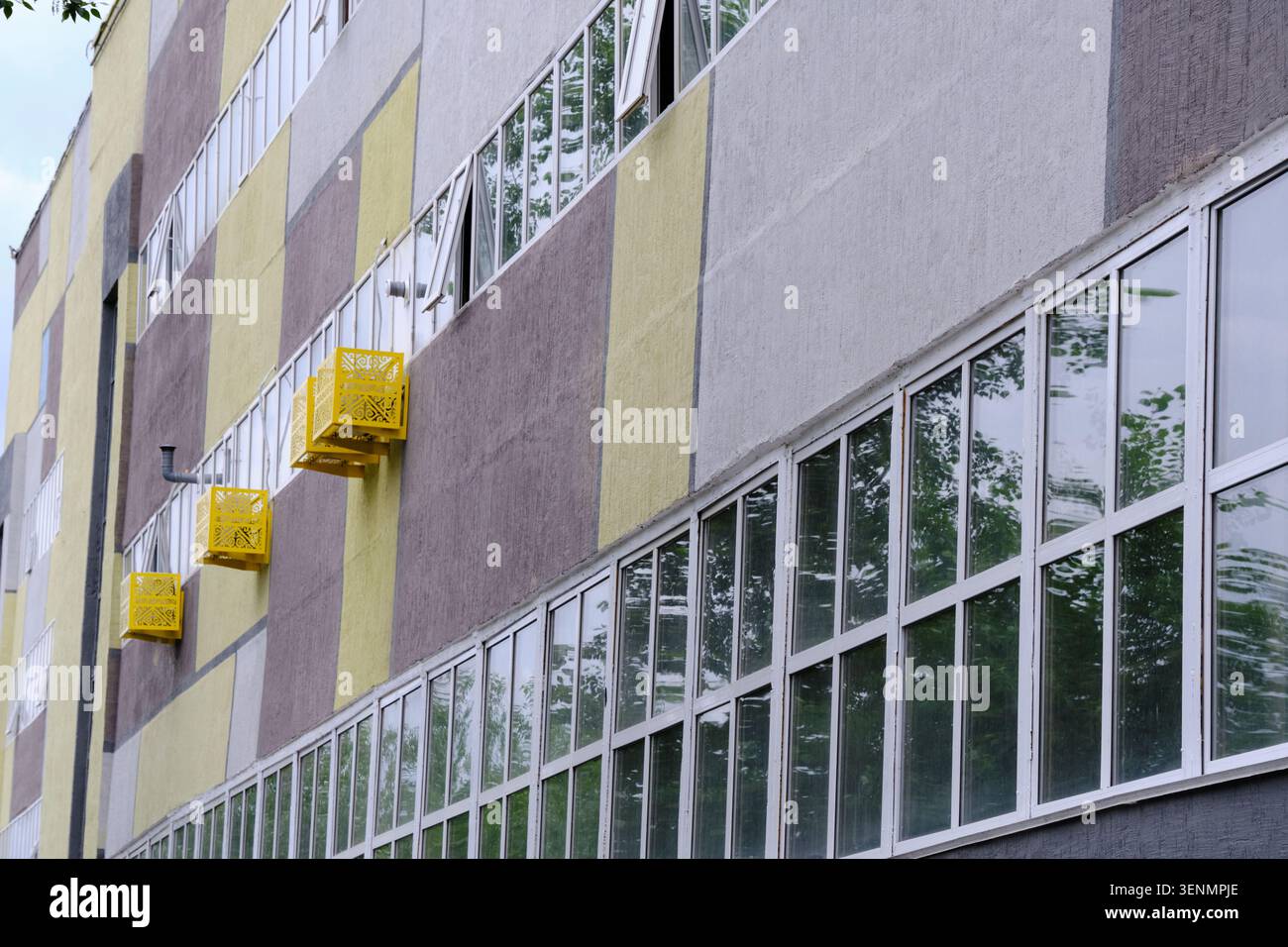 Facciata moderna di un edificio industriale con grandi finestre in vetro ed elementi decorativi gialli per condizionatori d'aria Foto Stock