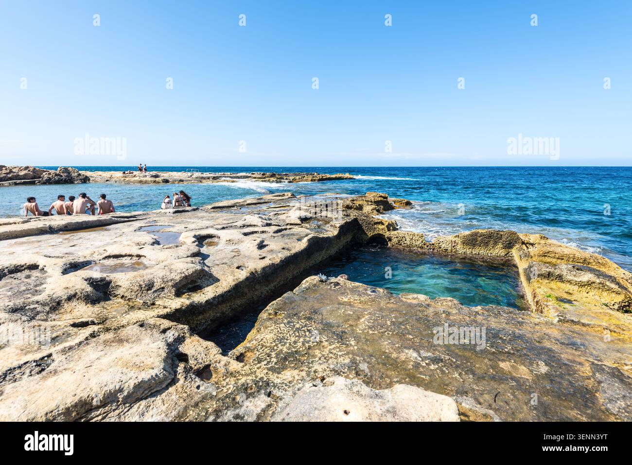 Sliema, Malta - 16 maggio 2025: Persone che si rilassano presso la costa rocciosa delle terme romane a Sliema, Malta, godendosi il sole, il turchese wat del Mediterraneo Foto Stock