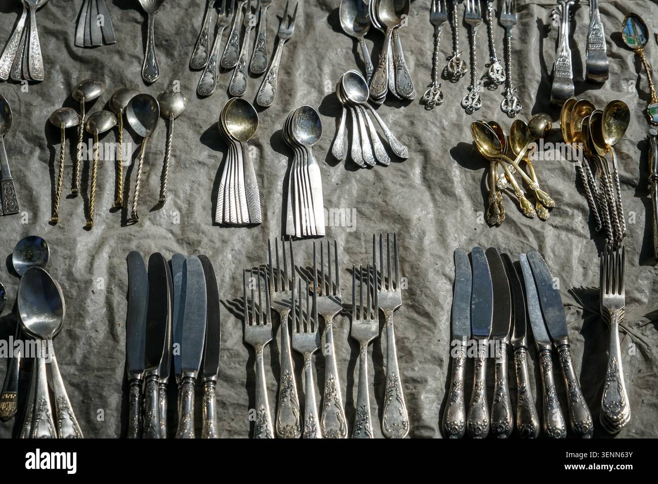 Una vasta collezione di posate antiche e vintage, tra cui forchette, cucchiai e coltelli, è meticolosamente disposta su una superficie in tessuto grigio. Gli ornati S Foto Stock