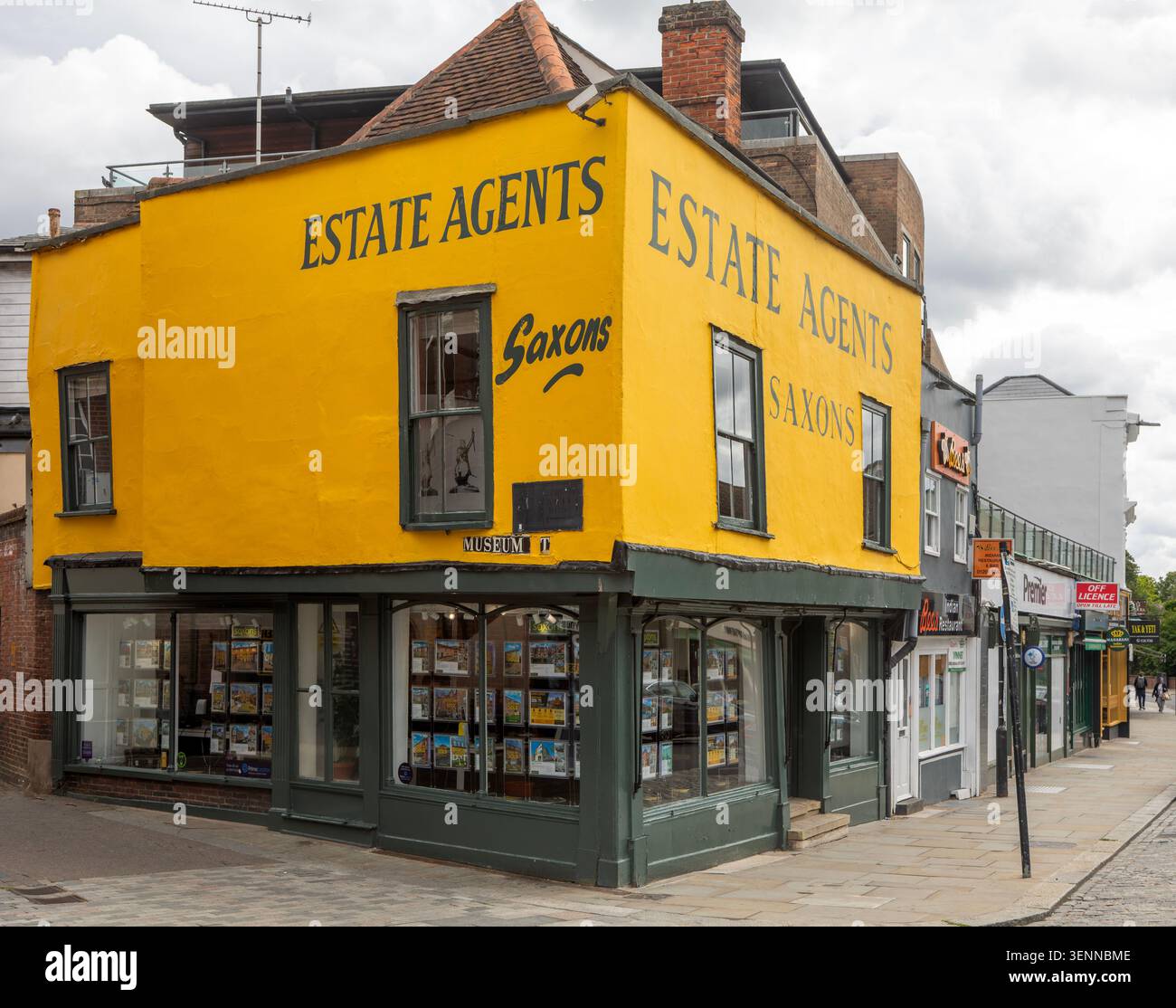 Edificio ad angolo giallo luminoso agente immobiliare Saxons, Museum Street e High Street, centro città di Colchester, Essex, Inghilterra, Regno Unito Foto Stock