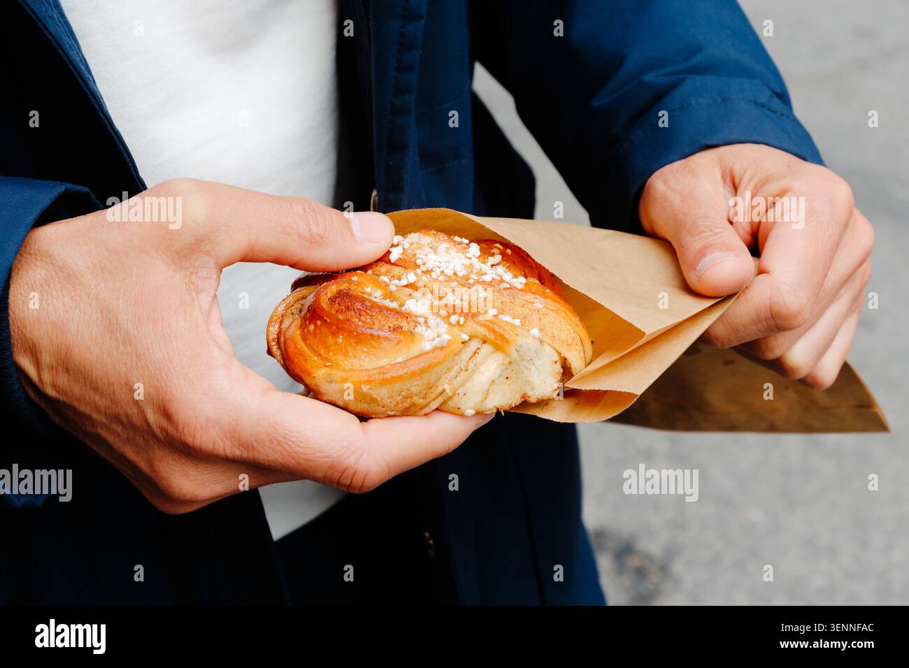 un uomo srotola una cannella, il tradizionale panino svedese alla cannella, da un sacchetto di carta marrone, tenendo la pasta ricoperta di zucchero perlato durante una sosta Foto Stock