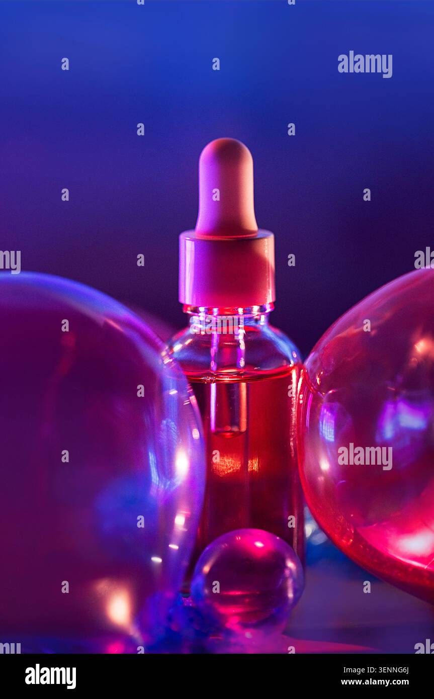 Il flacone contagocce in vetro contenente siero rosa è posizionato tra sfere traslucide, illuminate da effetti di luce blu e viola sullo sfondo Foto Stock