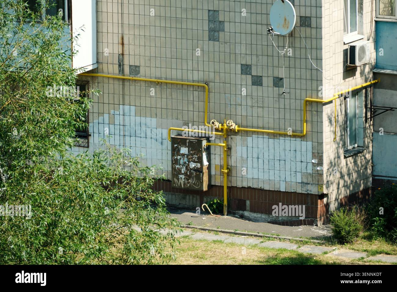 Vista ravvicinata dell'esterno di un edificio residenziale di appartamenti con gasdotti gialli per gas naturale, attrezzature di servizio, facciata piastrellata e infrastrutture urbane Foto Stock
