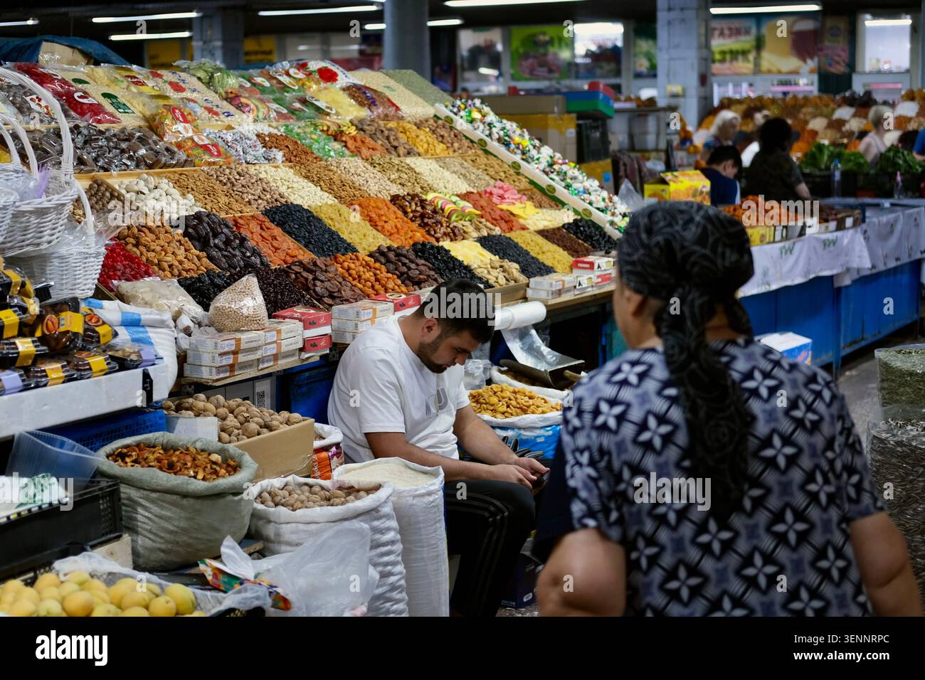 Almaty, Kazakistan - giugno 2026: Un venditore tende a un mercato pieno di frutta secca, noci e semi presso il Green Bazaar di Almaty, Kazakistan. Foto Stock