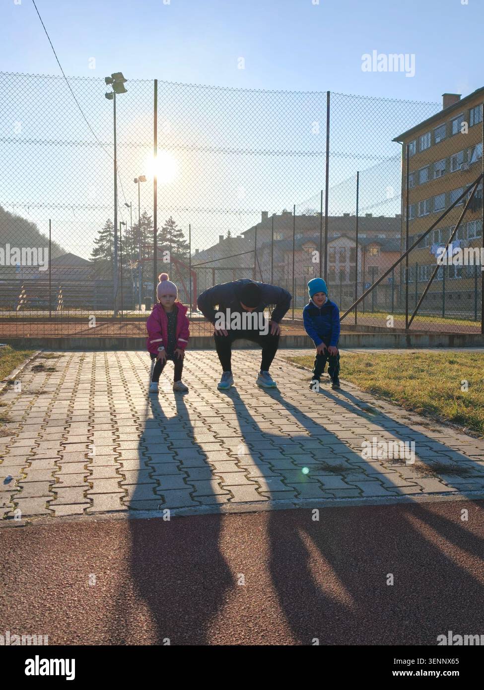 Padre coaching bambini che fanno squat di riscaldamento sul campo sportivo all'aperto al tramonto Foto Stock