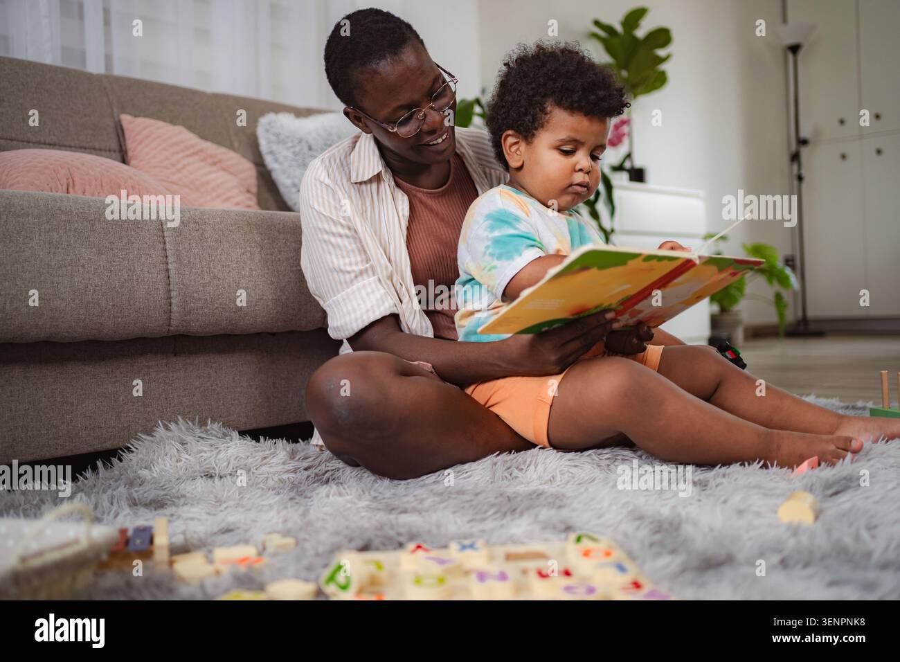 La madre e il bambino leggono insieme un libro sul pavimento di casa Foto Stock