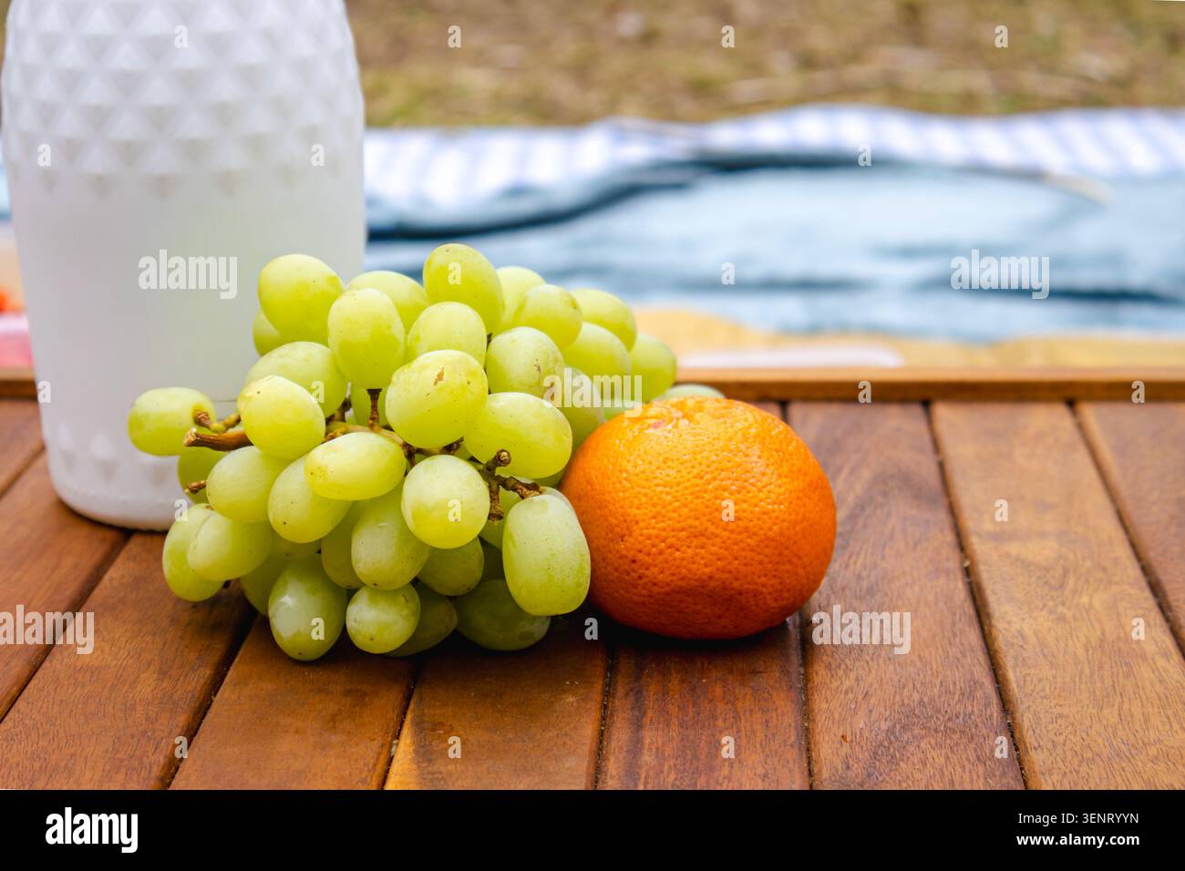 Uva fresca e arancia su un tavolo da picnic in legno all'aperto. Snack semplici e salutari, cibo naturale e informale concetto di ristorazione all'aperto. Foto Stock