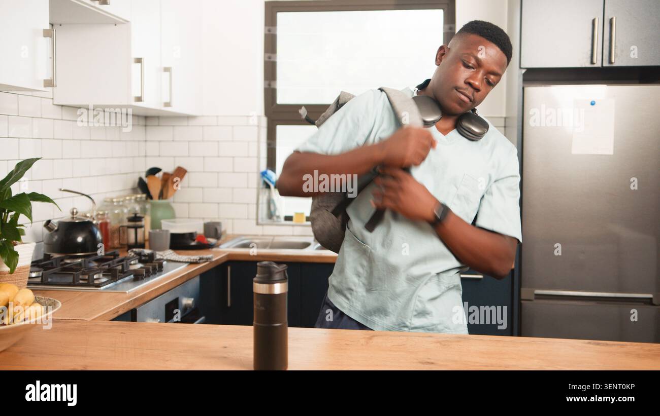 Giovane lavoratore sanitario che lascia la cucina con zaino e tazza da viaggio prima del turno di mattina Foto Stock