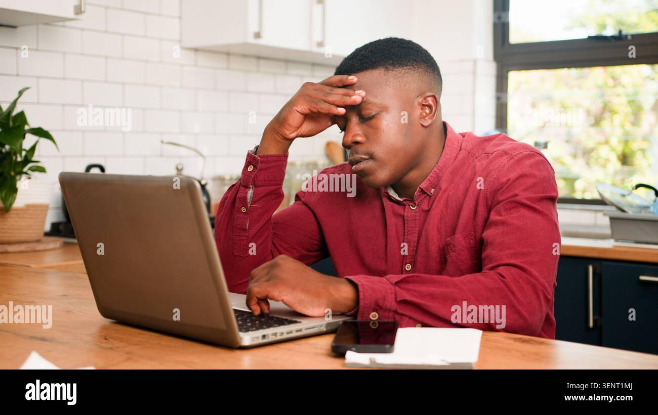 Giovane stressato che lavora su un laptop in cucina Home Office sfregamento Forehead Foto Stock