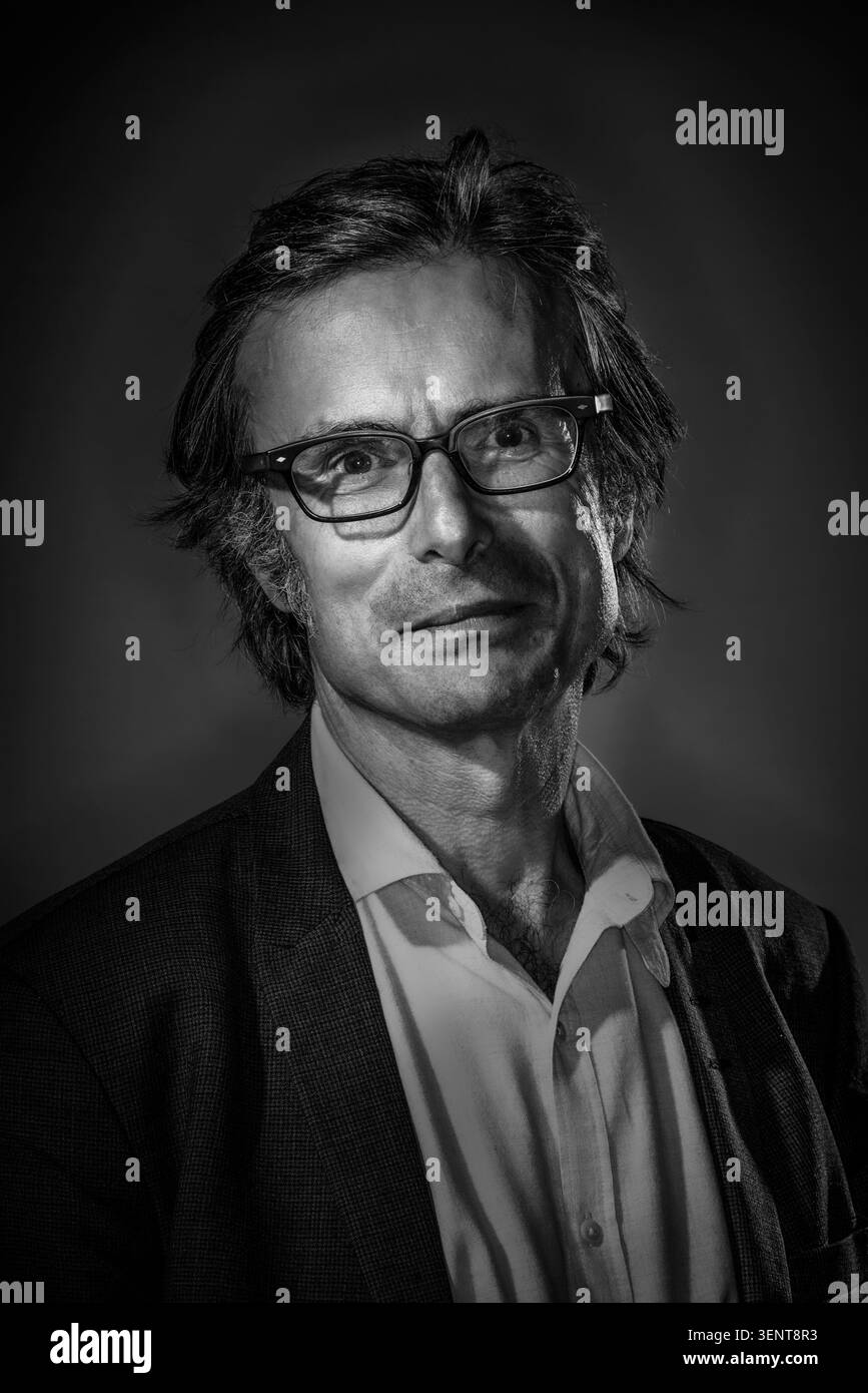 Robert Peston posa per un ritratto. Indossa occhiali e un vestito scuro con una camicia bianca. L'illuminazione crea delle ombre sul suo volto. Il reema di sfondo Foto Stock