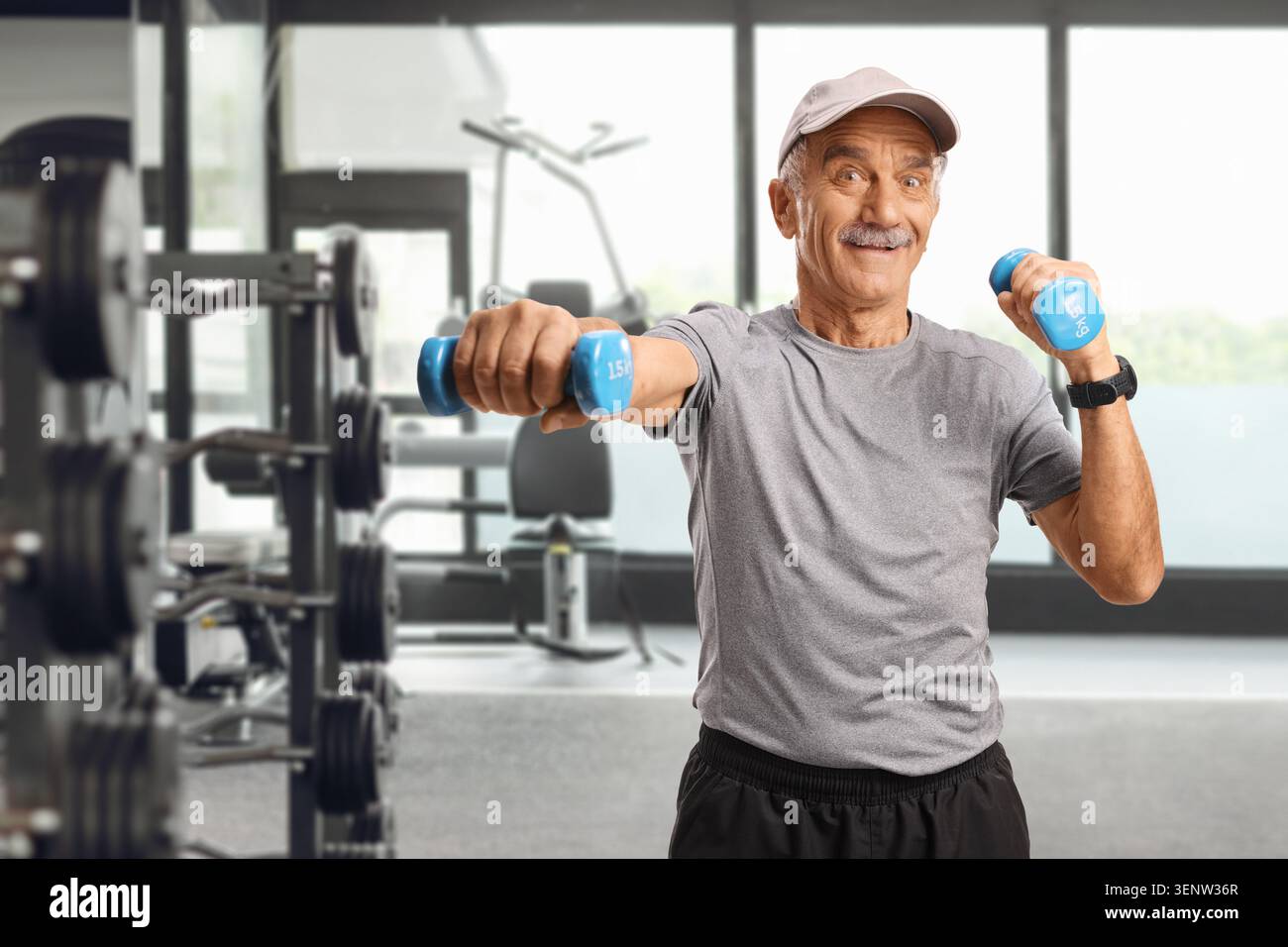 Uomo anziano attivo che fa esercizio con manubri in palestra e sorride Foto Stock
