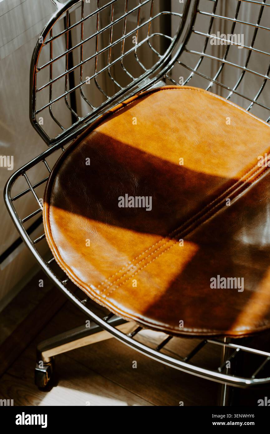 Sedia in pelle marrone con struttura in filo cromato alla luce del sole calda, mobili d'epoca lucidi con linee geometriche e tessuti interni moderni Foto Stock